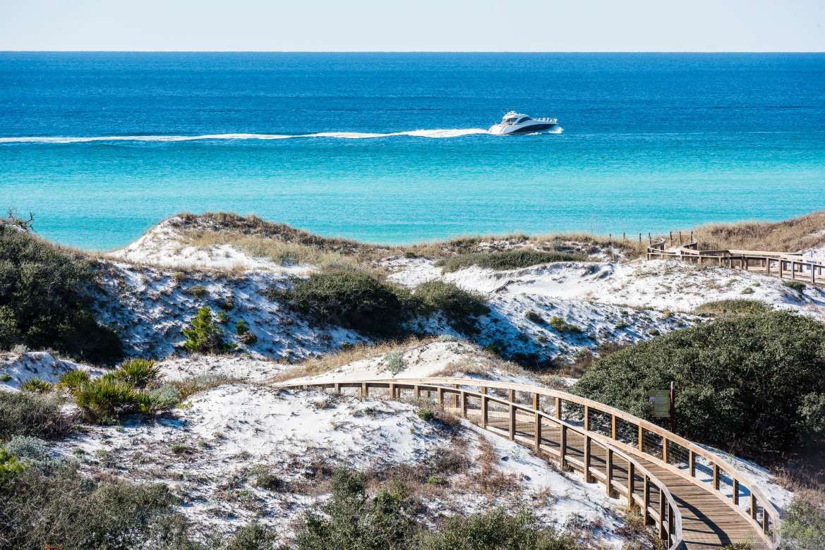 Wooden boardwalk winding over white sand dunes toward emerald Gulf water in WaterSound, 30A, FL